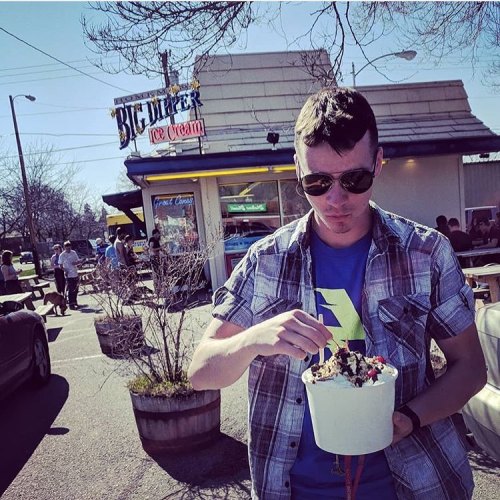 A person enjoying a large ice cream sundae outside an ice cream shop on a sunny day.
