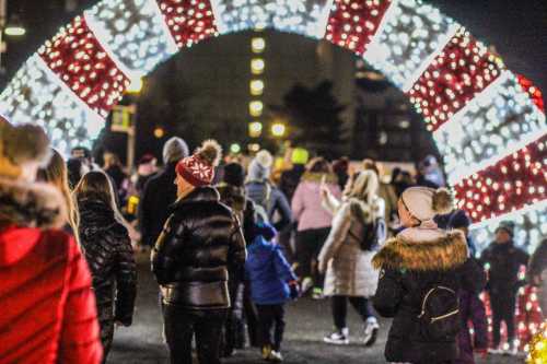 A festive archway adorned with red and white lights, with a crowd of people walking underneath at night.