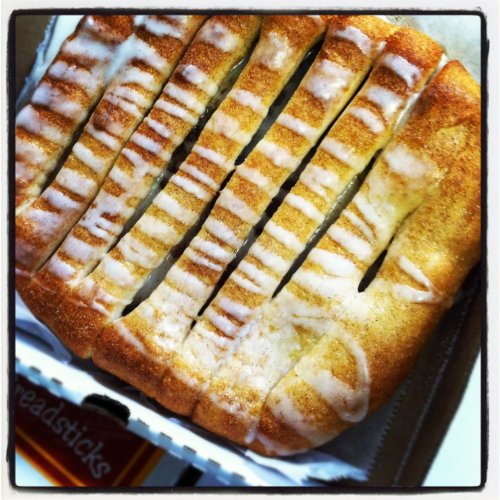 A golden-brown dessert with a glazed topping, sliced into strips, resting in a takeout box.