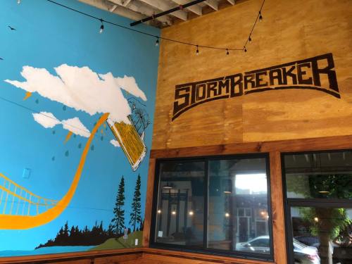 Interior of a restaurant featuring a mural with clouds, trees, and the word "STORMBREAKER" in bold letters on the wall.
