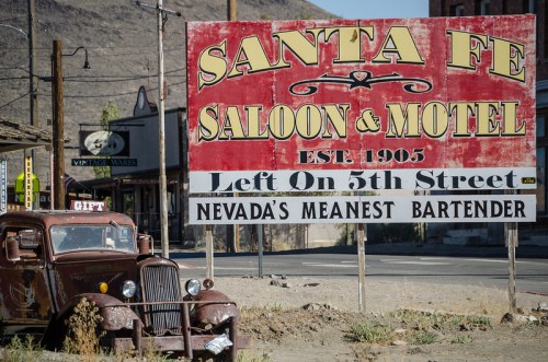 A vintage car parked near a weathered sign for the Santa Fe Saloon & Motel, established in 1905, in a desert town.