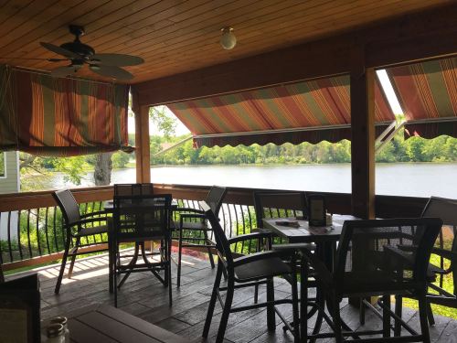 A cozy outdoor dining area with wooden furniture and striped awnings, overlooking a serene lake.