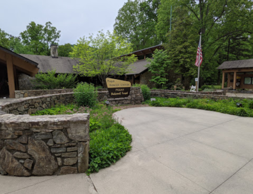 Entrance to a visitor center with stone walls, greenery, and an American flag in a national forest setting.