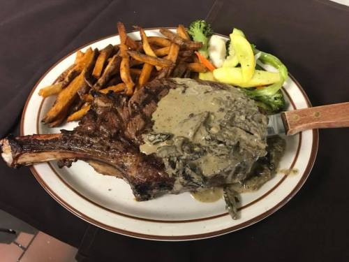 A large ribeye steak topped with creamy sauce, served with sweet potato fries and mixed vegetables on a plate.