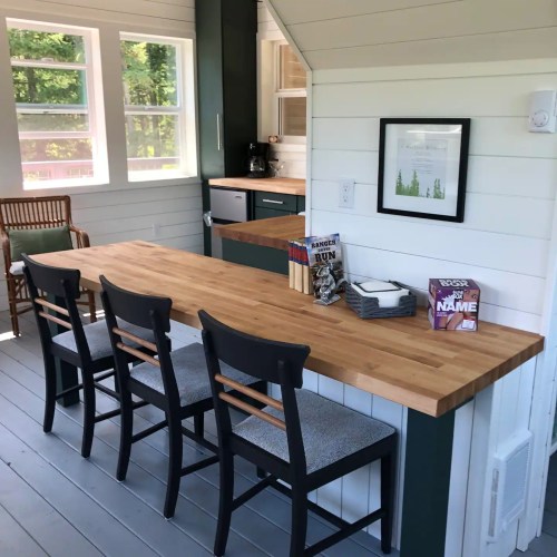 A cozy kitchen with a wooden table and four chairs, featuring a bright, airy design and large windows.