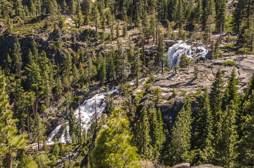 Aerial view of cascading waterfalls surrounded by lush green trees and rocky terrain.