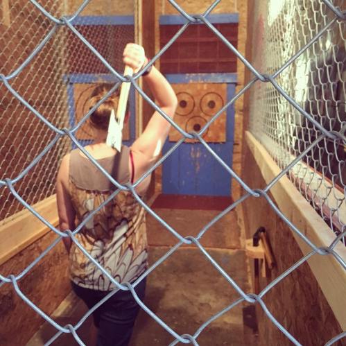 A person stands in an axe-throwing venue, preparing to throw an axe at a wooden target.