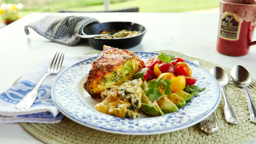 A plate of frittata with avocado and cherry tomatoes, accompanied by a coffee mug and a napkin on a table.