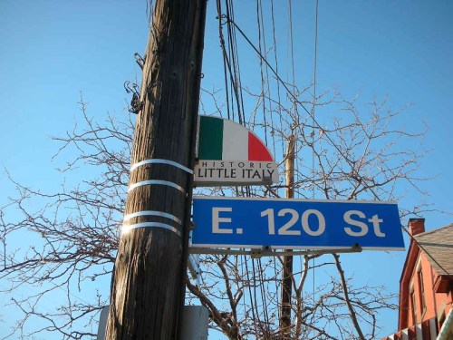 Sign for Historic Little Italy at E. 120 St. with a tree and utility pole in the background against a clear blue sky.