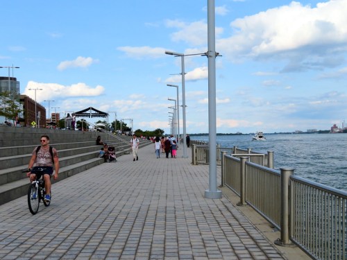 A waterfront promenade with people walking, biking, and enjoying the view of the water and sky.