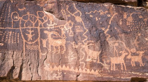 Ancient rock art featuring various symbols and figures, including animals and geometric patterns on a stone surface.