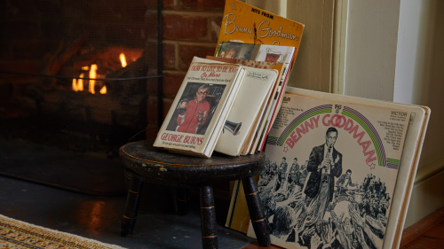 A small stool by a fireplace holds vintage music albums, including works by Benny Goodman and George Burns.