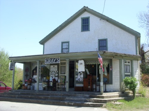A quaint, two-story shop with a porch, displaying a sign that reads "Gray's" and various items for sale outside.