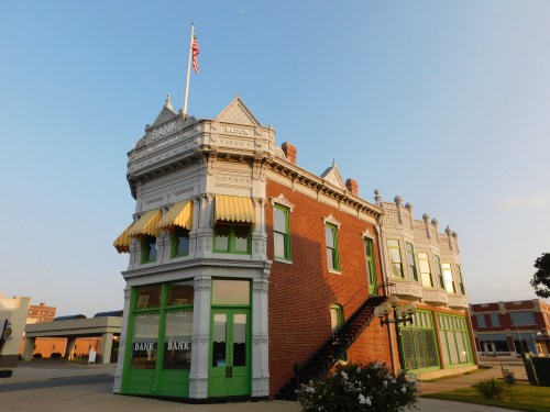 Historic bank building with ornate architecture, green accents, and a flag, set against a clear blue sky.