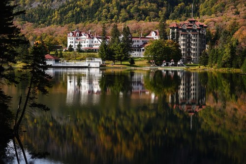 A scenic view of a lakeside hotel surrounded by autumn foliage, reflecting in the calm water.