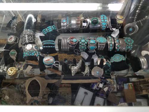 Display of various turquoise jewelry pieces, including bracelets, rings, and necklaces, arranged in a glass case.