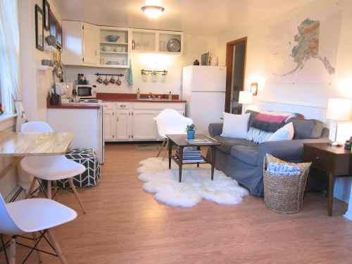 Cozy kitchen and living area with a sofa, dining table, and warm decor, featuring light wood floors and soft rugs.