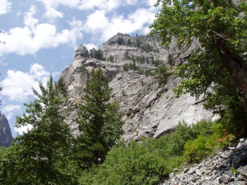 Rocky cliffs rise above lush greenery under a partly cloudy sky, showcasing a serene natural landscape.