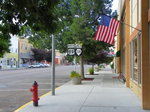 A quiet street scene with an American flag, a fire hydrant, and a bike near a sign for highways 89 and 221.