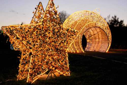 A large illuminated star and a glowing arch, both decorated with lights, set against a twilight sky.