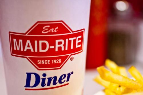 A close-up of a Maid-Rite Diner cup with fries in the background, featuring the diner’s logo and establishment year.