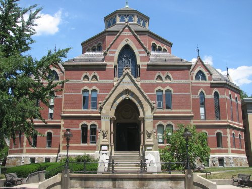 Historic red brick building with a domed roof, large arched entrance, and decorative windows, surrounded by greenery.