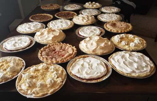 A table filled with various pies, featuring whipped cream and different fruit fillings, arranged in a festive display.
