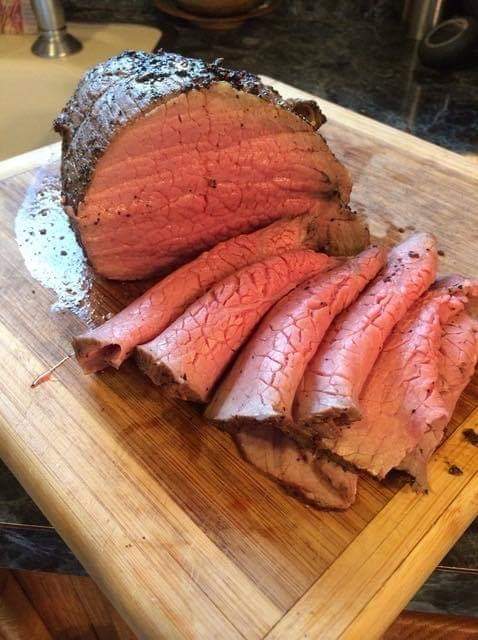 Sliced roast beef on a wooden cutting board, showcasing a juicy pink interior and a seasoned crust.