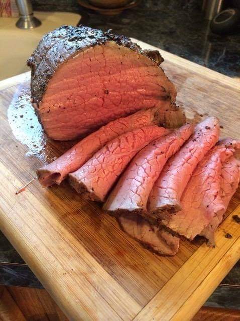 Sliced roast beef on a wooden cutting board, showcasing a juicy pink interior and a seasoned crust.