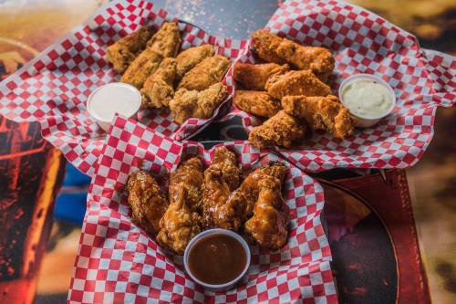 Two baskets of chicken wings with dipping sauces, served on red and white checkered paper.