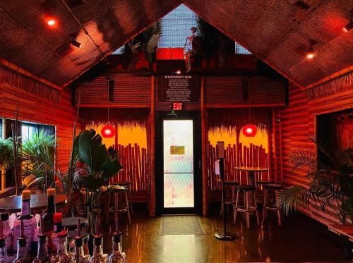 Cozy interior of a tropical-themed bar with wooden decor, plants, and warm lighting. Exit door visible at the back.