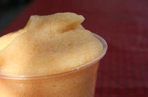 A close-up of a yellow slushy drink in a clear cup, with a smooth, frosty texture.