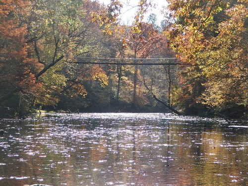 A serene river surrounded by colorful autumn foliage and a wooden bridge in the background.