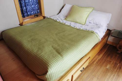 A neatly made bed with a green blanket and a decorative pillow, set in a cozy room with wooden accents.