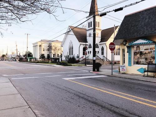 A quiet street scene featuring a church, a stop sign, and a small shop with a bench nearby.