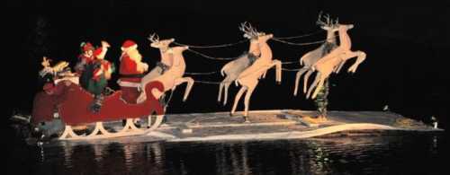 A festive scene of Santa and his reindeer on a decorated sleigh floating on water at night.