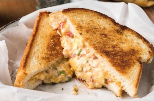 A toasted sandwich with melted cheese and colorful vegetables oozing out, served on parchment paper.