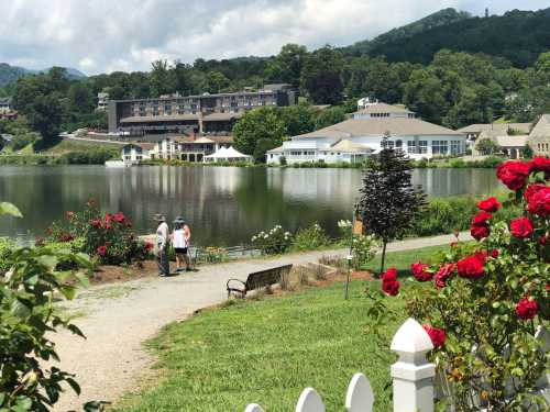 A serene lake view with a hotel in the background, surrounded by greenery and blooming roses along a walking path.