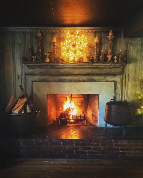 Cozy fireplace with a warm fire, surrounded by rustic decor and a glowing wreath on the mantel.