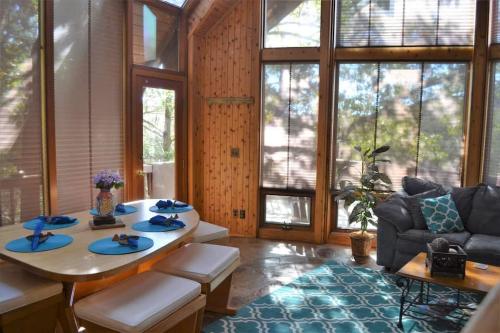 Bright sunroom with wooden walls, a dining table set for six, a cozy couch, and large windows letting in natural light.