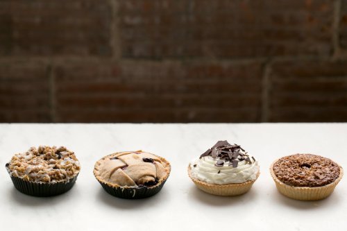 Four assorted desserts on a marble surface: a crumbly pie, a fruit-filled pastry, a cream-topped tart, and a chocolate treat.