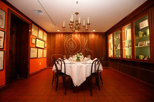 A cozy dining room with a white tablecloth, elegant table settings, and warm lighting, featuring art on the walls.