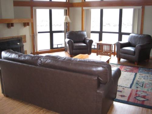 Cozy living room with large windows, two armchairs, a sofa, and a wooden coffee table on a patterned rug.