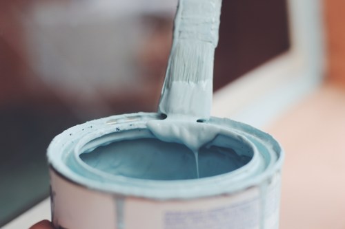 A paintbrush dipped in light blue paint, hovering over an open paint can.