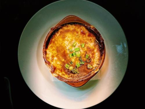 A baked dish with a golden, cheesy top, garnished with green onions, served in a brown ceramic bowl on a white plate.