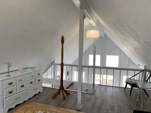 Bright attic space with sloped ceiling, wooden furniture, and a cozy atmosphere. Windows allow natural light.