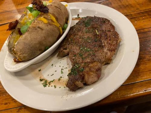A plate featuring a grilled steak and a loaded baked potato topped with cheese, bacon, and green onions.