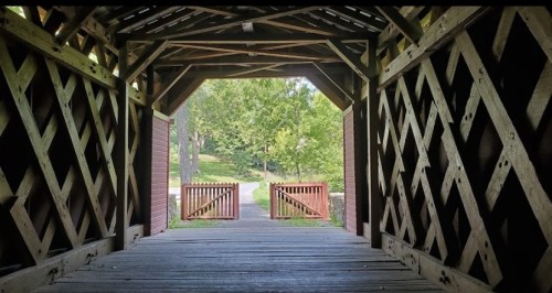 View from inside a covered bridge, looking out towards a green landscape and open gates.