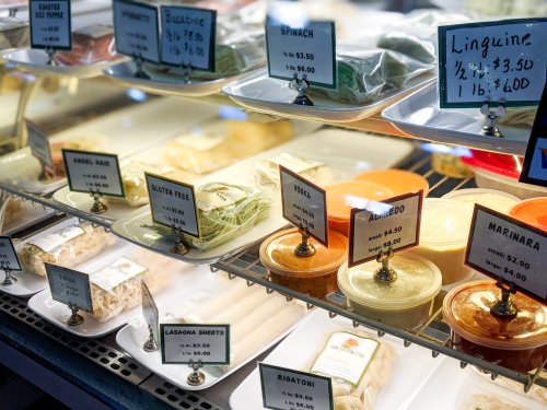 A display of various pasta types and sauces with price tags in a deli case.