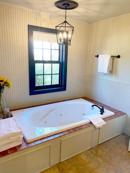 A bright bathroom featuring a white jacuzzi tub, a window with a black frame, and neatly arranged towels.